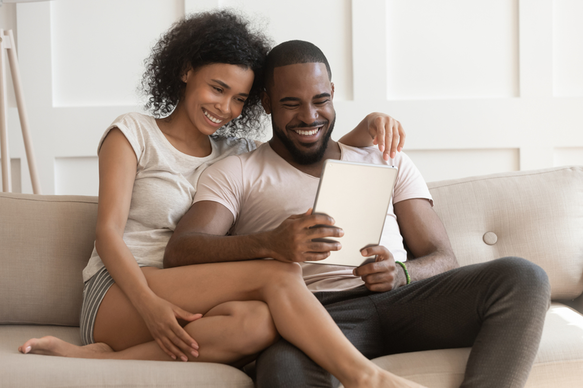 Happy couple sitting on a couch looking at a tablet screen together.
